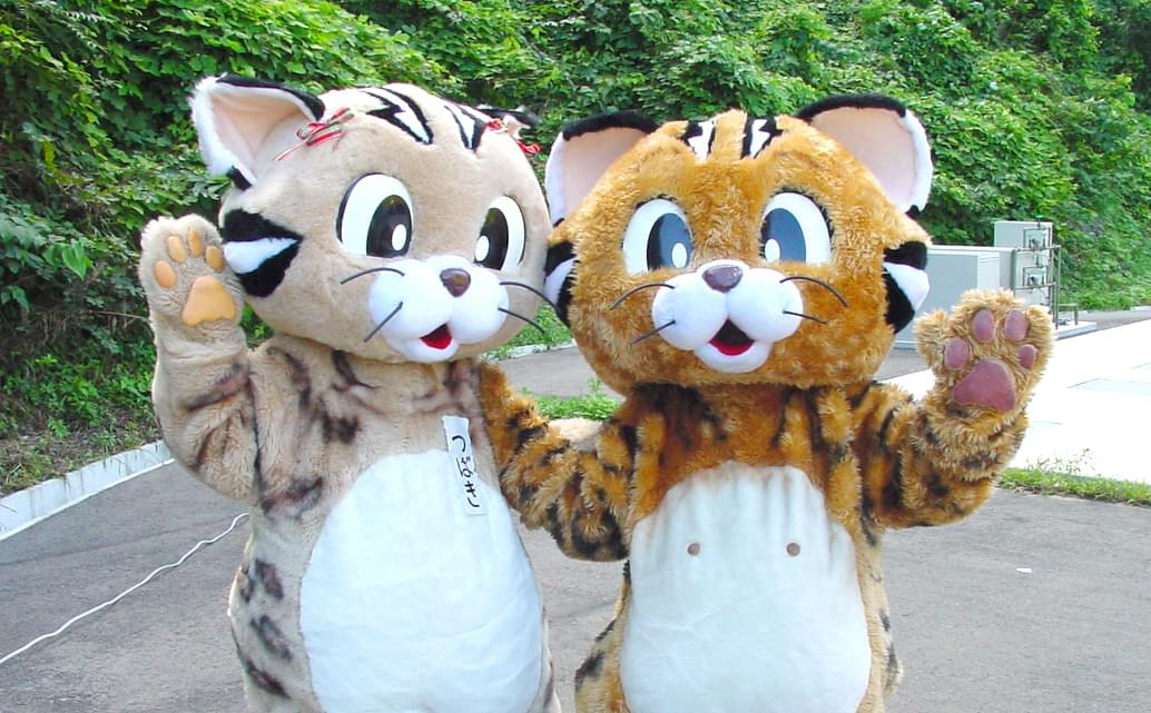 2体のツシマヤマネコの着ぐるみを着用して手を振っている、ヤマネコのイベントで撮られた写真。
