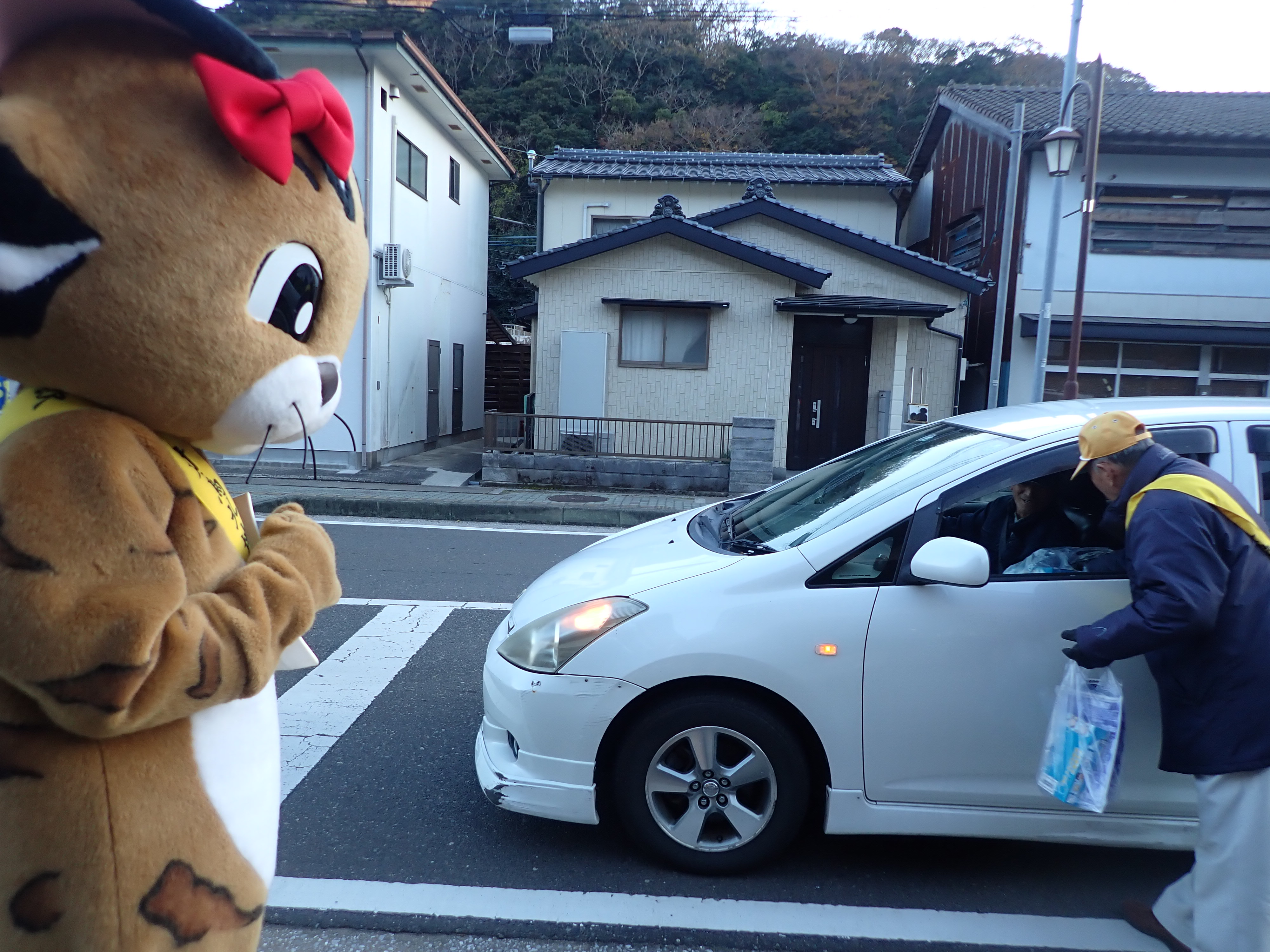 車を留めているドライバーに対して、ヤマネコの着ぐるみを着た職員が運転の注意喚起をしている様子の写真